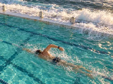Swimmer mid freestyle in an ocean pool beside breaking surf