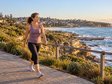 Woman walking beside the Coogee coastal rail in warm morning light